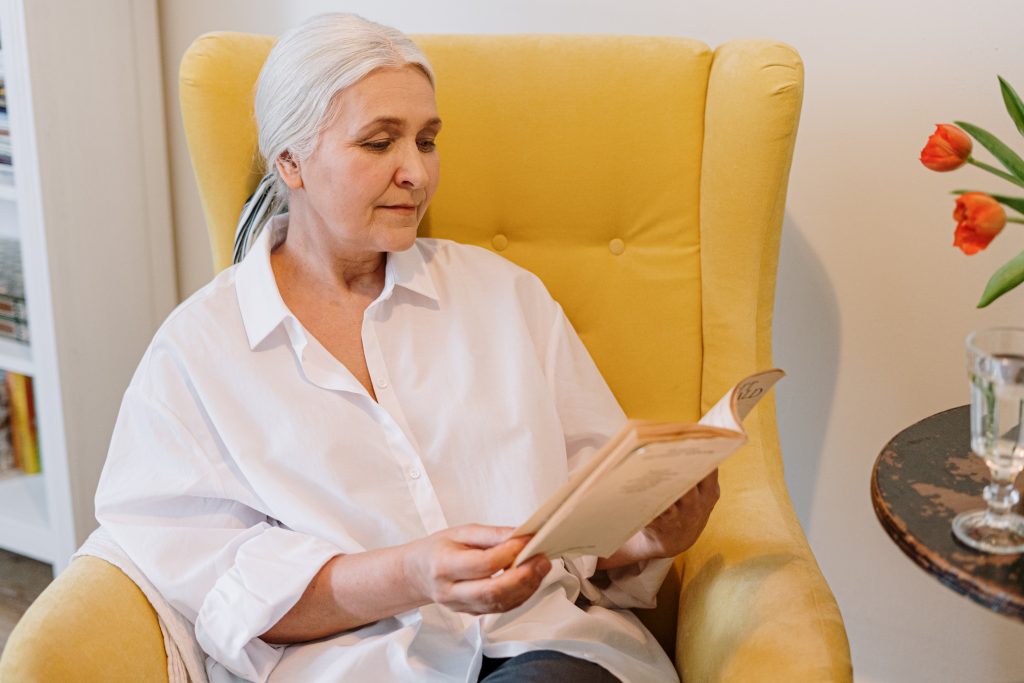 an-elderly-woman-sitting-on-a-couch-reading-a-book-4057763