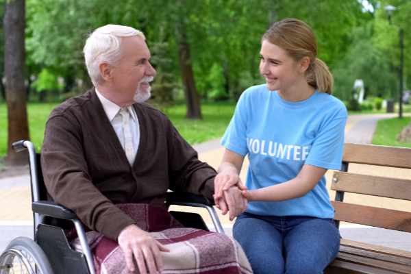 young girl in a Volunteer tshirt sitting with elderly man who is in a wheelchair